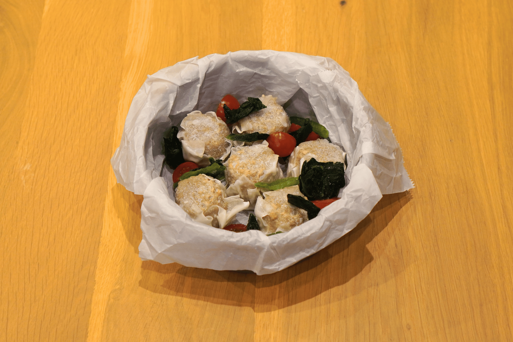 耐熱容器にクッキングシートをしき、凍ったままの大阪王将 たれつき肉焼売と、①のミニトマト、冷凍ほうれん草を入れる。