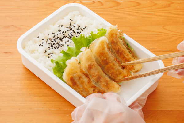 弁当箱に冷ましたご飯を詰め、いりごまをふる。ご飯の端に水気をよくとったレタスを敷き、焼き餃子を立てかけるように並べる。